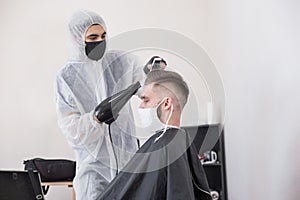 The work of the barber during the coronavirus, the hairdresser trim the client in a mask and a protective suit, quarantine