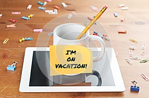 Work and business concept: a cup with a pencil inside on a tablet with a memo and the text I`m on vacation