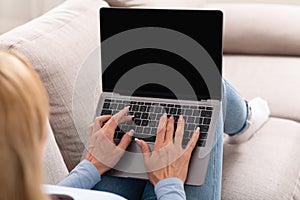 Work on couch. Woman is typing on laptop with blank screen, sitting on sofa