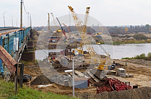 The work of cranes and other equipment at the construction site of the bridge across the river