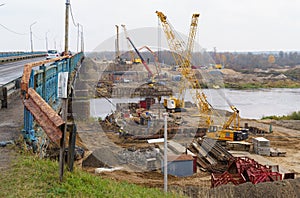 The work of cranes and other equipment at the construction site of the bridge across the river