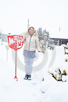 Work at the dacha in winter, a lot of snow. A girl with a shovel cleans the snow in the village.