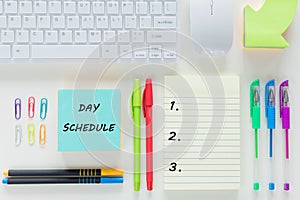 Work day plan.  A card with the words Day Schedule, pens, a computer keyboard, a notebook with a blank page ready to be saved.  Vi