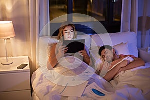 Woman with tablet computer working in bed at night