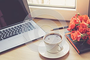 Work desk interior with a laptop computer and morning coffee cup. Toned photo of female work desk with computer and coffee cup.