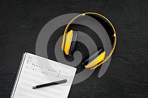 Work desk of modern composer. Music notes near headphones on black background top view copy space