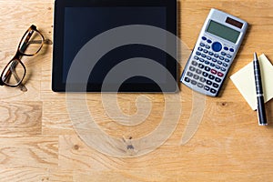 Work desk with tablet, glasses, calculator and notepad on wooden