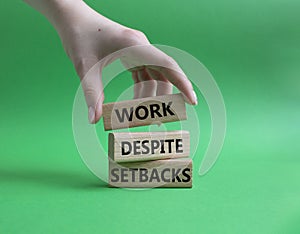 Work despite setbacks symbol. Wooden blocks with words Work despite setbacks. Beautiful green background. Businessman hand.