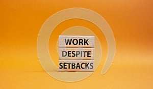 Work despite setbacks symbol. Wooden blocks with words Work despite setbacks. Beautiful orange background. Business and Work