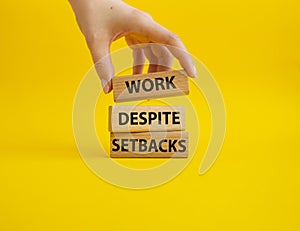 Work despite setbacks symbol. Wooden blocks with words Work despite setbacks. Beautiful yellow background. Businessman hand.