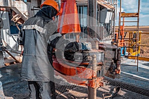 Work driller in red uniform, in helmet and goggles. He uses a hydraulic wrench to screw drill pipes to lower them into an oil well