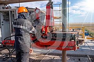 Work driller in red uniform, in helmet and goggles. He uses a hydraulic wrench to screw drill pipes to lower them into an oil well