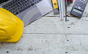 work environment with a laptop, a yellow hard hat, calculator, level, screwdriver, and folding ruler on a well-used wooden surface