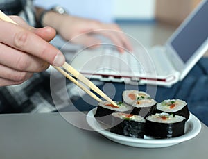 Work and Food Man working on Laptop taking Sushi