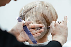 The work of a hairdresser. Hairdresser cut hair of a woman. Close-up of hands and tool.