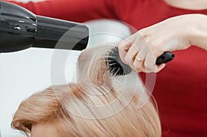 The work of a hairdresser. The master dries the client`s hair using brushing. Close-up of hands and tool