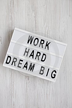 `Work hard dream big` words on a lightbox on a white wooden background, top view. Flat lay, overhead, from above