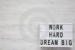 `Work hard dream big` words on a lightbox on a white wooden background, top view. Flat lay, overhead, from above. Copy space
