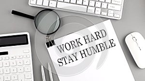 WORK HARD STAY HUMBLE written on paper with office tools and keyboard on the grey background