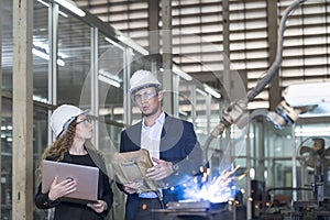 Work in a Heavy Industry Manufacturing Factory. Industrial man and woman engineer with laptop in control robot of factory