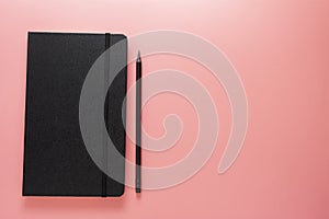 Work from home. Black notebook or journal with black pencil over pink background, flat lay, copy space