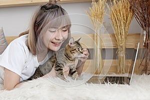 Work from home with cat. Young Asian woman playing with a cat in a living room with a laptop computer