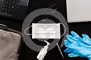 Work from home cleaning kit on black background office desk with hand sanitizer and face mask and gloves, against coronavirus