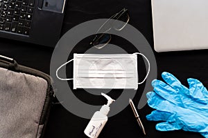 Work from home cleaning kit on black background office desk with hand sanitizer and face mask and gloves, against coronavirus photo