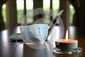 Work at home during coronavirus outbreak. Focus on face mask with computer laptop and burning candle on table