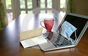 Work at home during coronavirus pandemic. Focus on face mask on computer laptop on the dining table