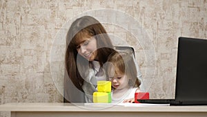 Work at home. in the room, mom works at the table with her little daughter at the computer. business woman working in