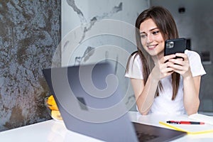 Work at home. A young woman use a laptop to work in the kitchen writes something in a notebook with a pen and speaks on the phone