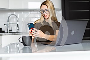 Work at home. Young woman use a laptop to work in the kitchen writes something in the phone