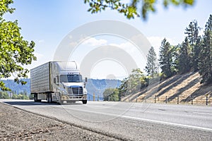 Work horse big rig semi truck transporting cargo in loaded refrigerator semi trailer driving on the mountain highway road in