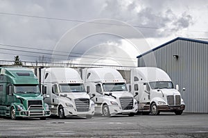 Work horses big rig semi trucks with semi trailers standing on the industrial parking lot waiting for the next load