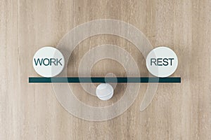 Work life balance concept with scales from board on a ball and equal weight plates with words work and rest on wooden background