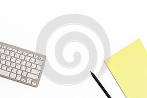 Work office desk with a keyboard, a yellow notepad and a black p