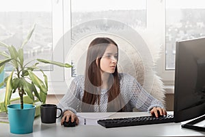 Work in the office. A young girl sits at a table typing on a computer