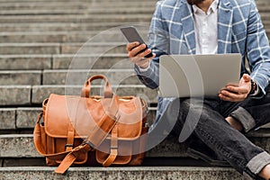 Work outdoors, a man sits on the stairs and works on a laptop and talking on the phone. Modern lifestyle