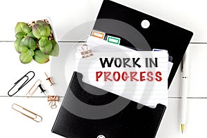 WORK IN PROGRESS text on note with office supplies