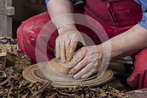 Work with red clay. Male hands form a bowl on a spinning pottery wheel.