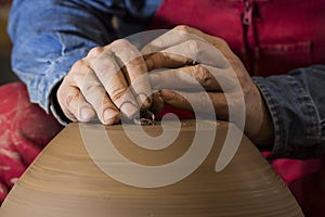 Work with red clay. Male hands form a bowl on a spinning pottery wheel.