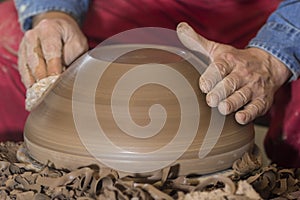 Work with red clay. Male hands form a bowl on a spinning pottery wheel.