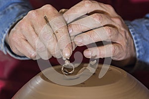 Work with red clay. Male hands form a bowl on a spinning pottery wheel.