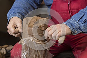 Work with red clay. Male hands form a bowl on a spinning pottery wheel.