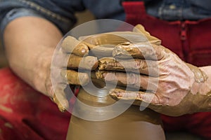 Work with red clay. Male hands form a bowl on a spinning pottery wheel.