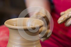 Work with red clay. Male hands form a bowl on a spinning pottery wheel.