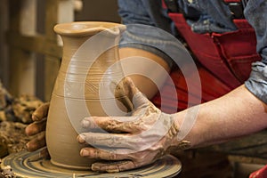 Work with red clay. Male hands form a bowl on a spinning pottery wheel.