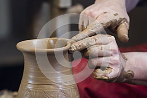 Work with red clay. Male hands form a bowl on a spinning pottery wheel.