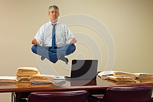 Work related stress relief with yoga as man hovering over stacks of paperwork and computer